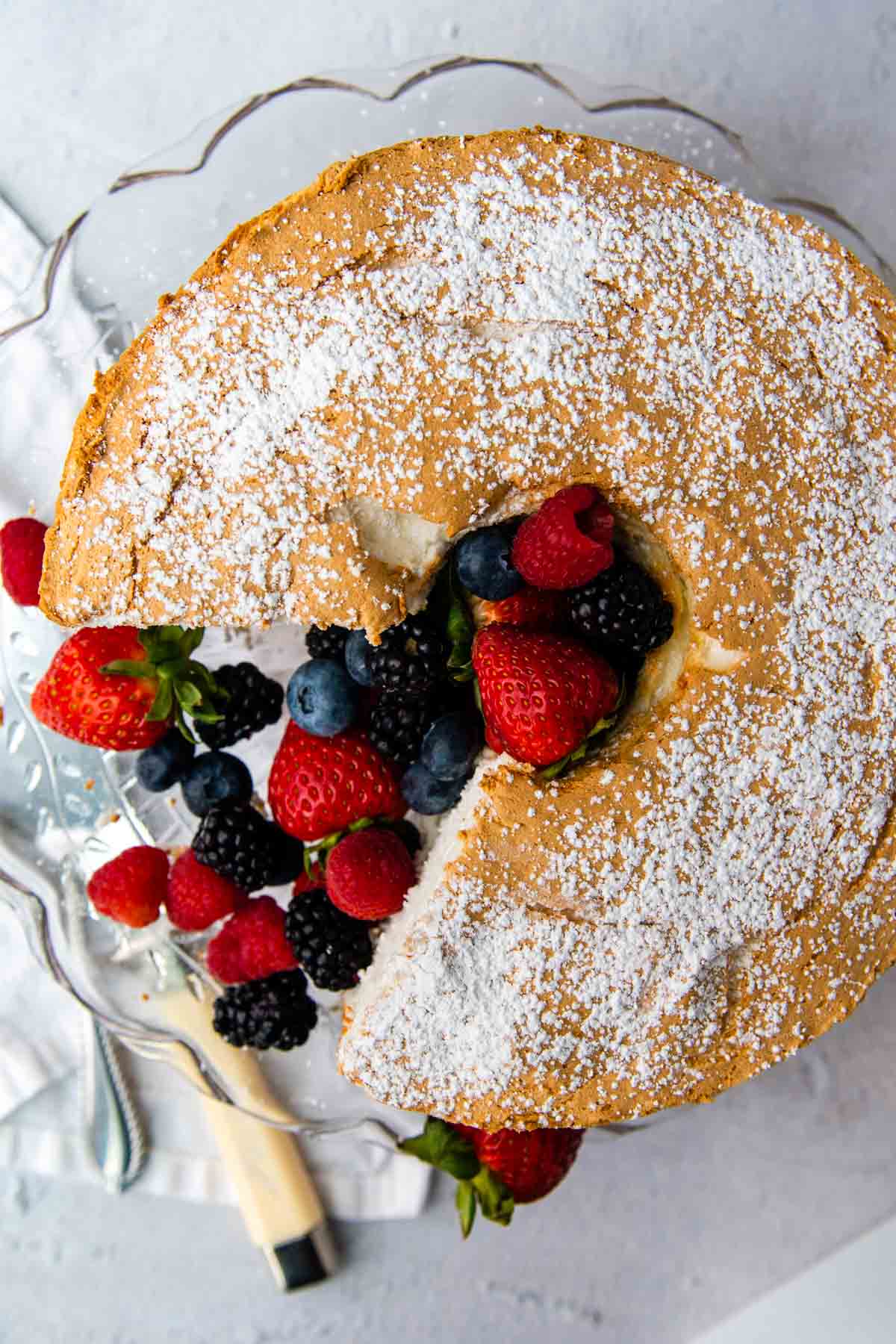 overhead shot of angel food cake with berries in the middle and a cake knife laying next to it.