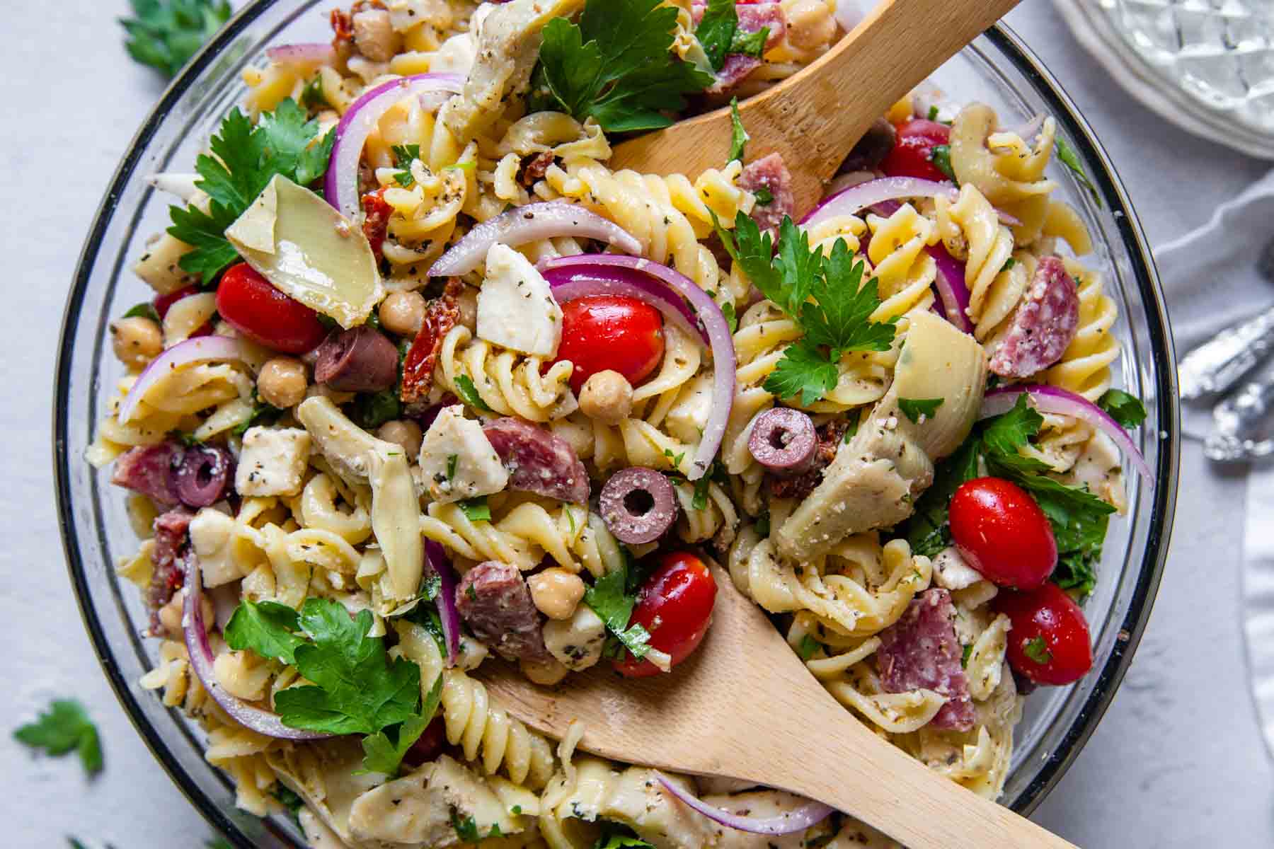 overhead shot of pasta salad with wooden spoons in bowl.