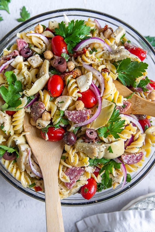 overhead shot of cold pasta salad with wooden spoons sticking out of bowl