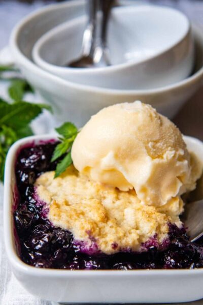 a single serving of fruit cobbler in a blue white square bowl with a scoop of ice cream on top