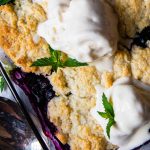 close up of top of gluten-free blueberry cobbler with melting ice cream on top and mint leaves
