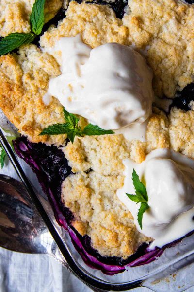 close up of top of gluten-free blueberry cobbler with melting ice cream on top and mint leaves