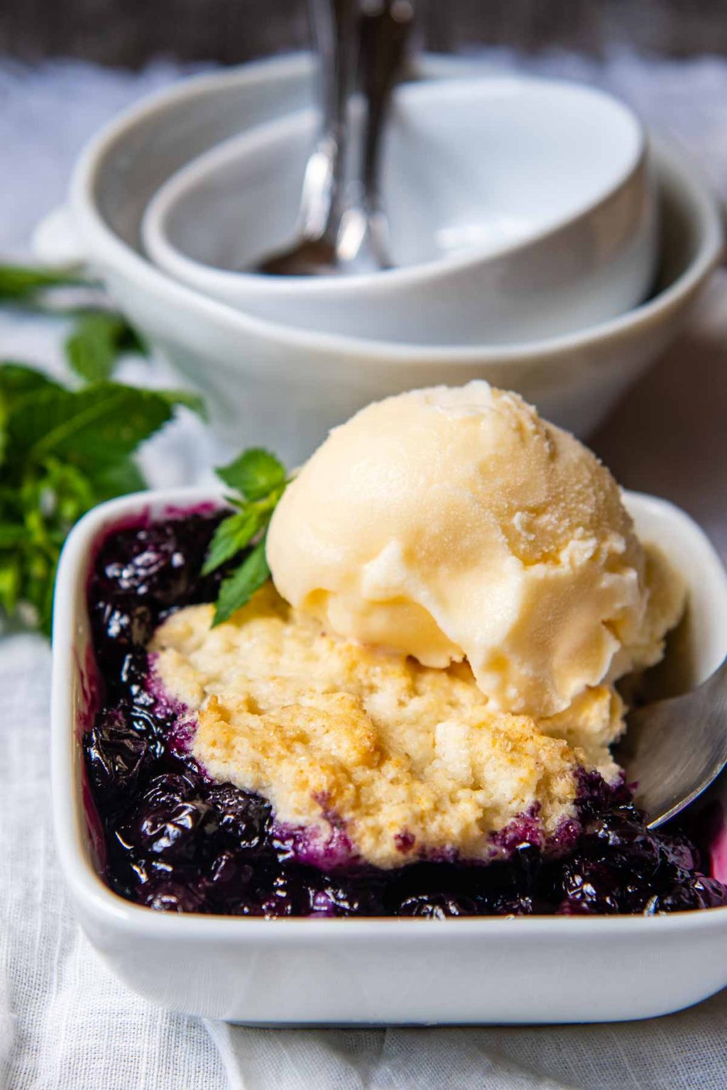 a single serving of fruit cobbler in a blue white square bowl with a scoop of ice cream on top