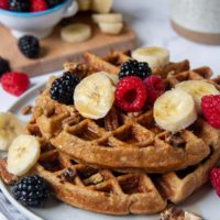 shot of gluten free waffles on a plate with berries, nuts, and bananas on top