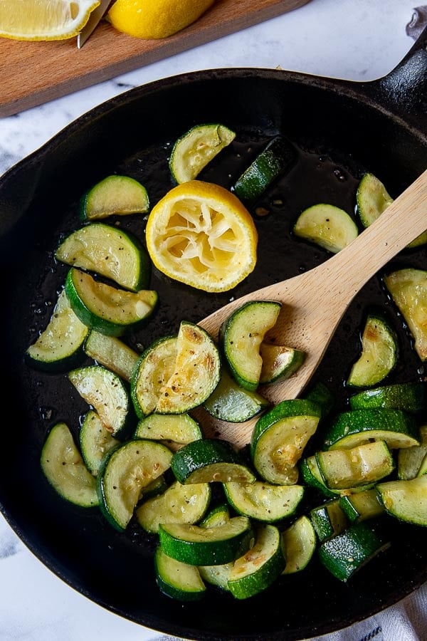 overhead shot of sauteed zucchini in a cast iron skillet with a squeezed lemon