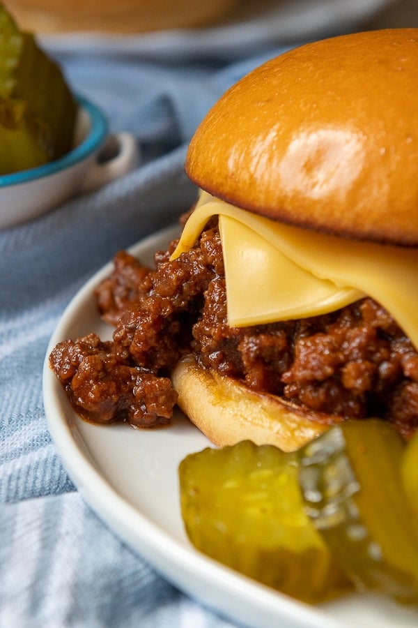 sloppy joe meat dripping out of a bun with pickles in the foreground