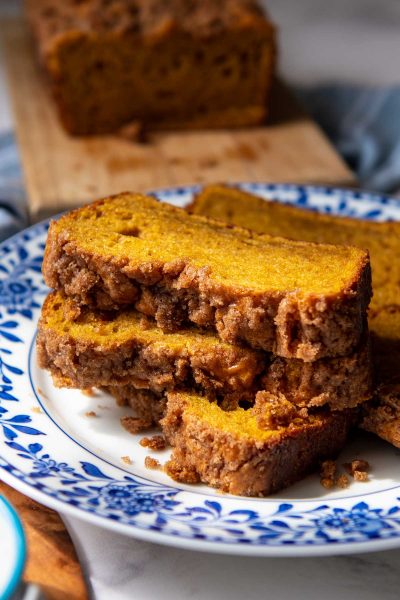 a stack of three slices of pumpkin bread with streusel topping on a blue and white flower plate
