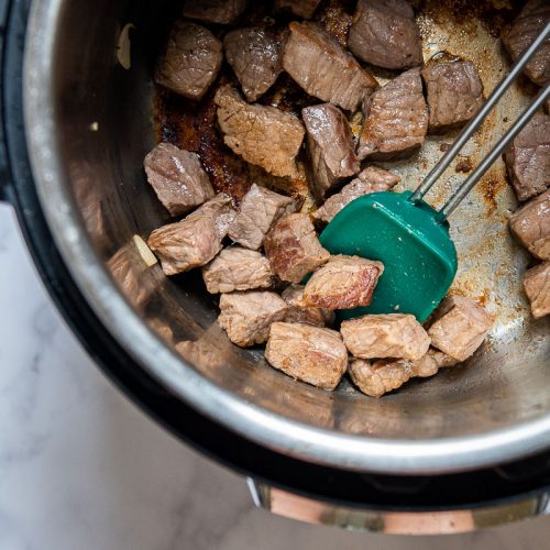 a green silicone spoon sauteing beef in a pressure cooker