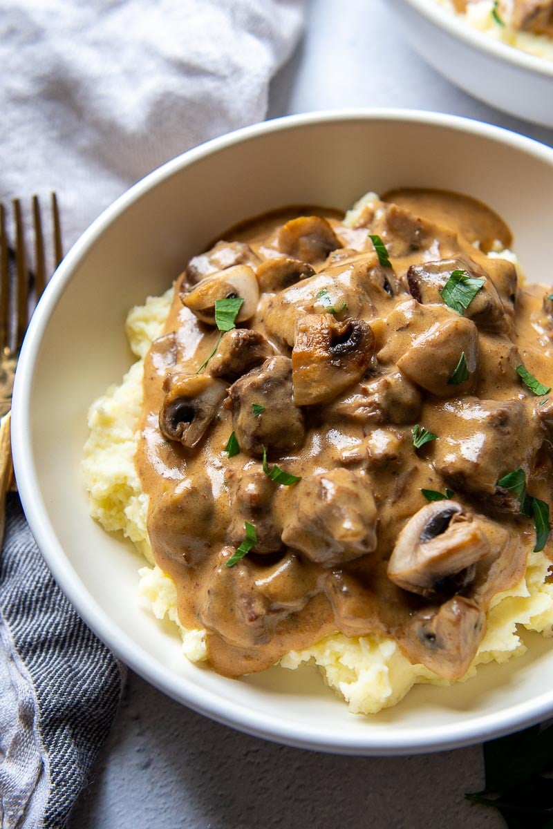 angled shot of a bowl of pressure cooker beef stroganoff served over mashed potatoes