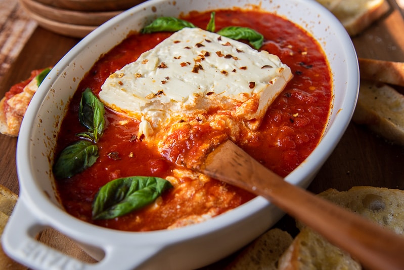 a wooden knife cutting into baked feta with tomato sauce underneath
