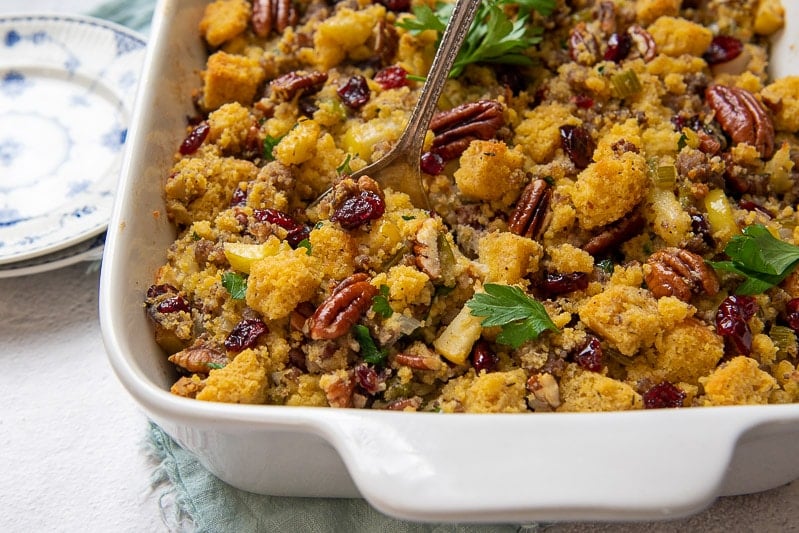 close up of gluten stuffing in a white baking dish with a spoon going in