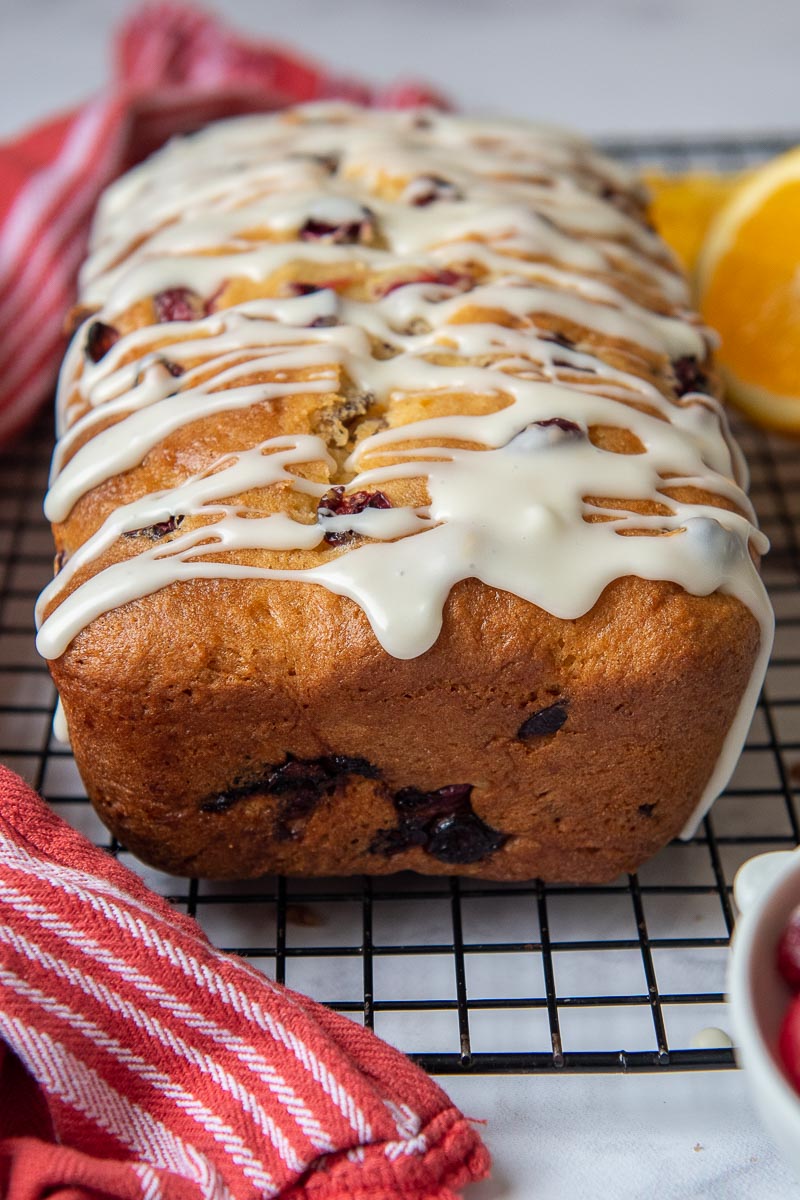 cranberry orange loaf on a cooling rack with a close up of edge with frosting dripping down