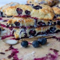 a stack of scones with fresh blueberries scattered around and spoon with frosting