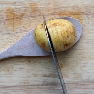 a knife cutting a potato into hasselback style