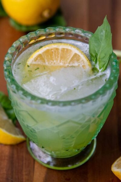 a gin basil smash cocktail in a green glass with a lemon wedge and basil garnish