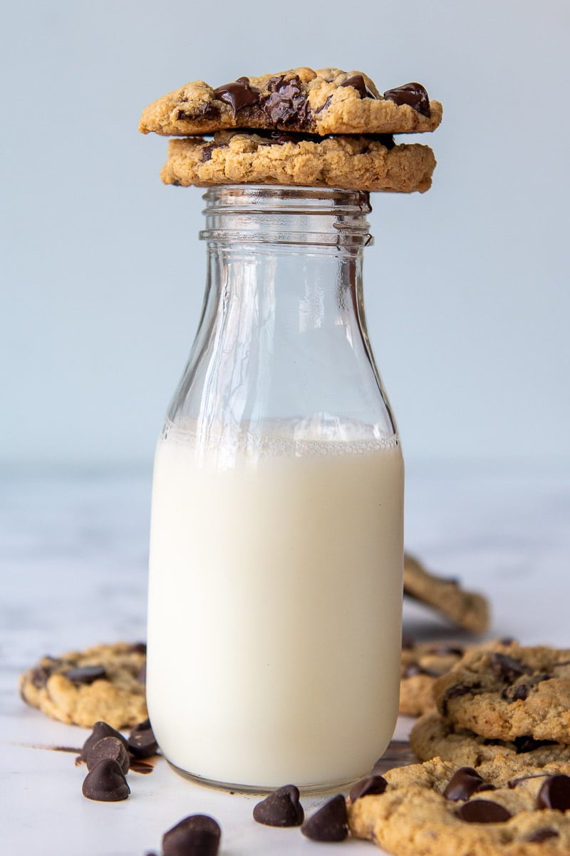 a chocolate chip cookie resting a tall glass of milk