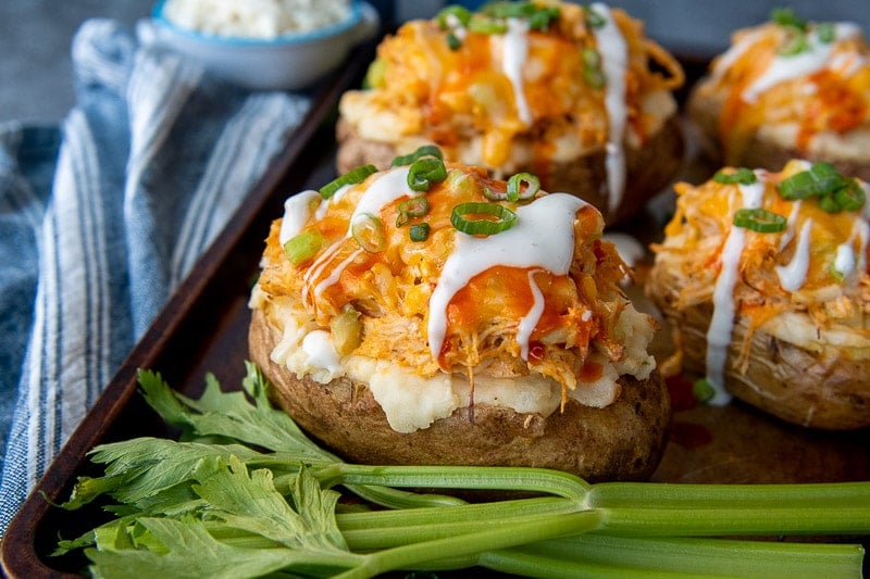 a twice baked potato on a baking sheet with celery sticks laying next to it and buffalo chicken topping