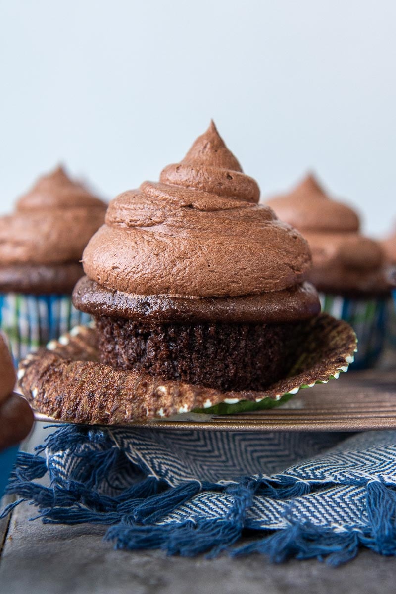 a chocolate frosted cupcake on a cooling rack partially unwrapped
