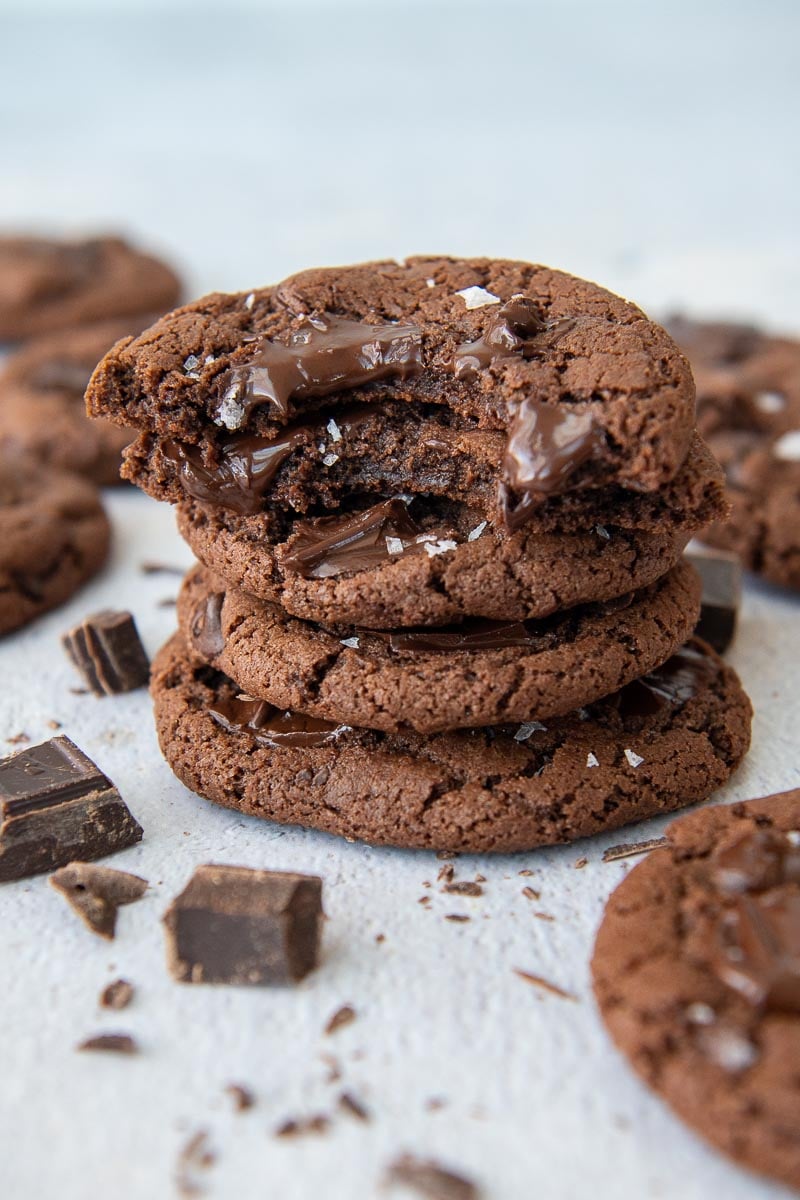 a stack of cookies with the top two having bites taking out and chocolate chunks laying around it