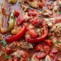 close up of baked chicken with peppers, mushrooms, and onions in a tomato sauce