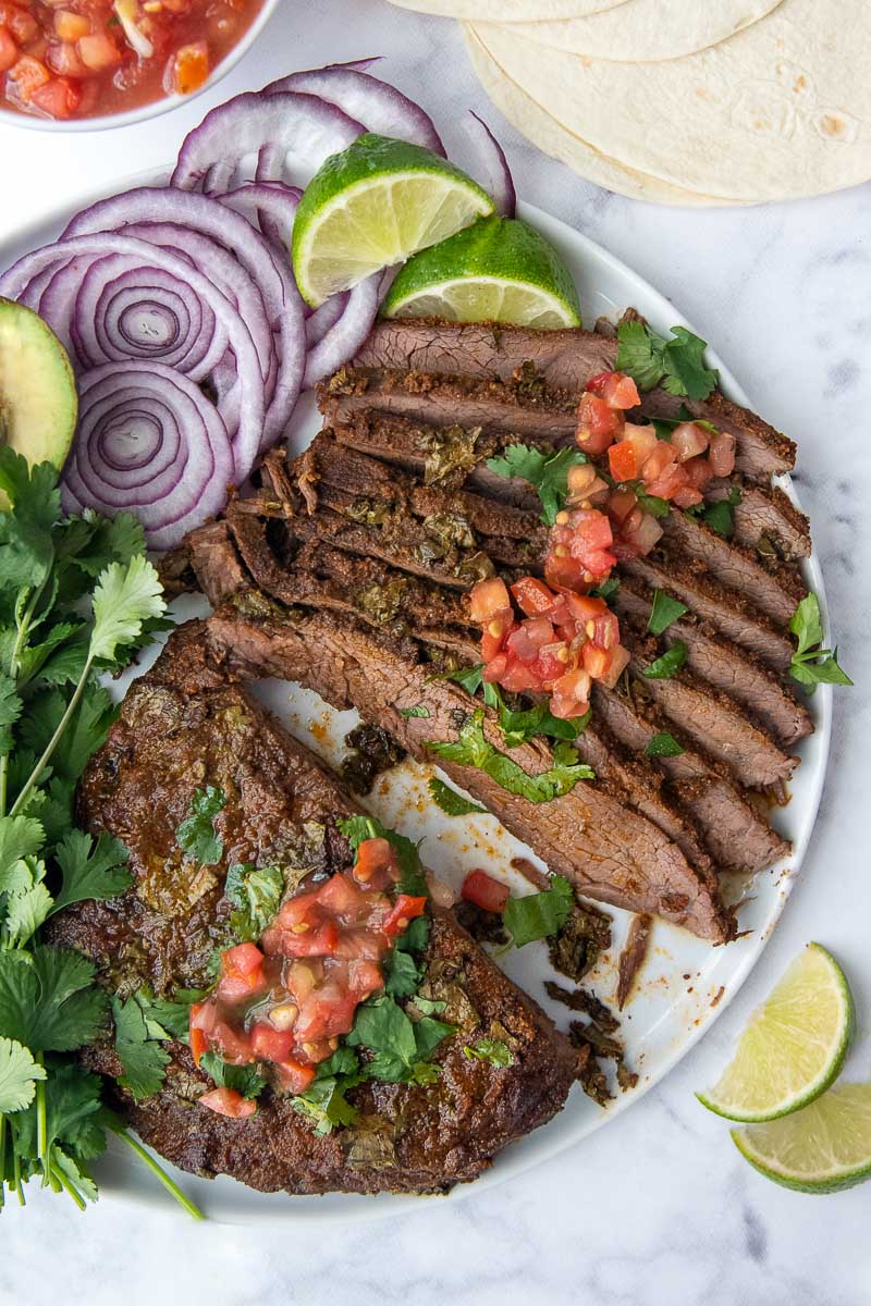 overhead shot of sliced carne asada with avocado, red onion, and limes laying next to it
