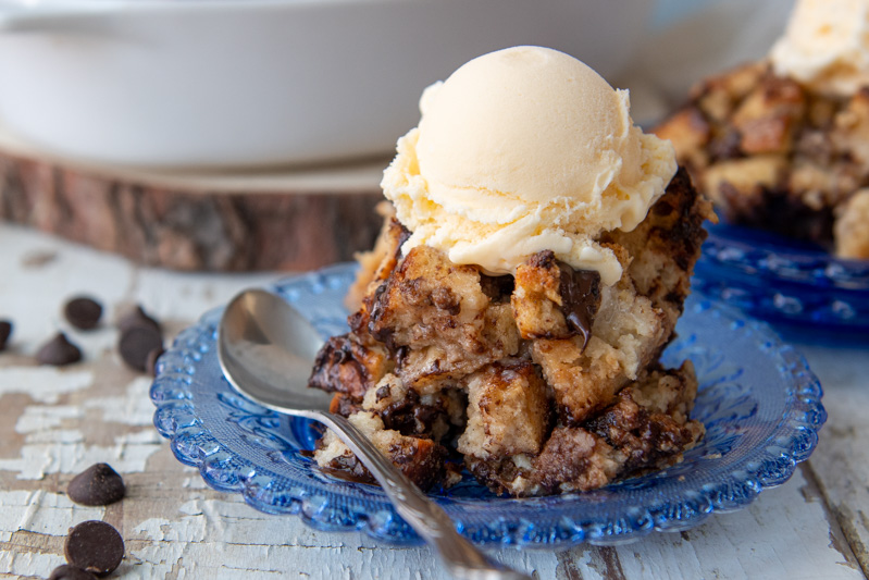 a serving of chocolate chip bread pudding on a blue plate with a scoop of melting ice cream on top