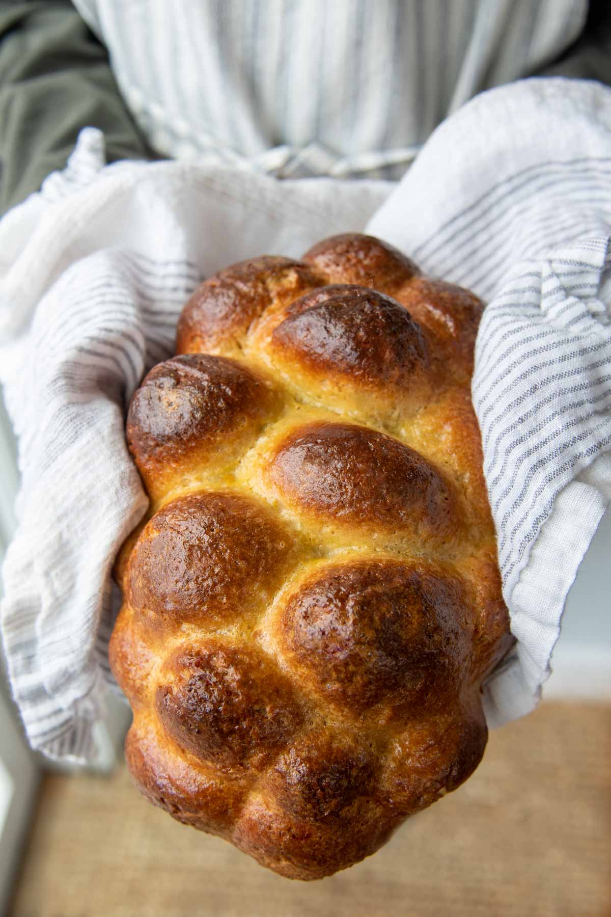 a uncut loaf of gluten free challah bread being held up by someone wearing an apron.