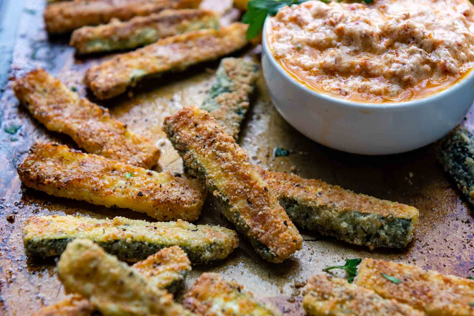 zucchini fries with a cup of dipping sauce in the background.