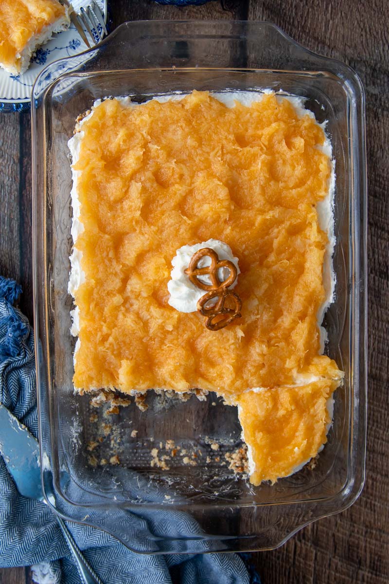 overhead shot of pineapple pretzel salad in a glass dish with a blue towel next to it