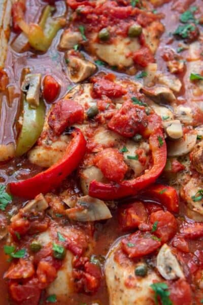 close up of baked chicken with peppers, mushrooms, and onions in a tomato sauce