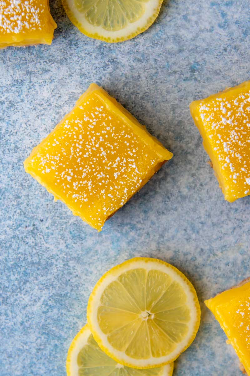 overhead shot of cut lemon bars on a blue background with sliced lemons next to it