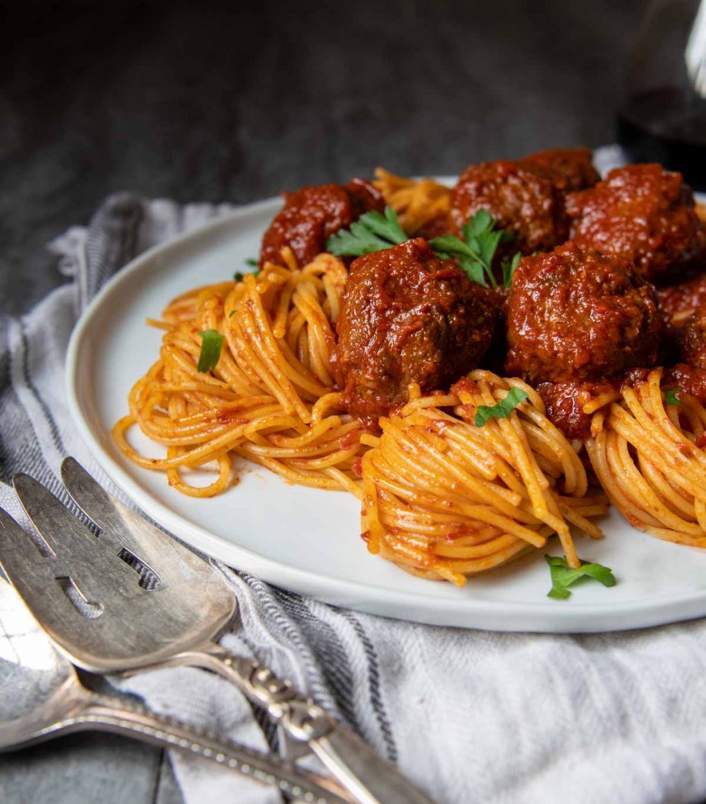 spaghetti and meatballs on a white plate with a dark background