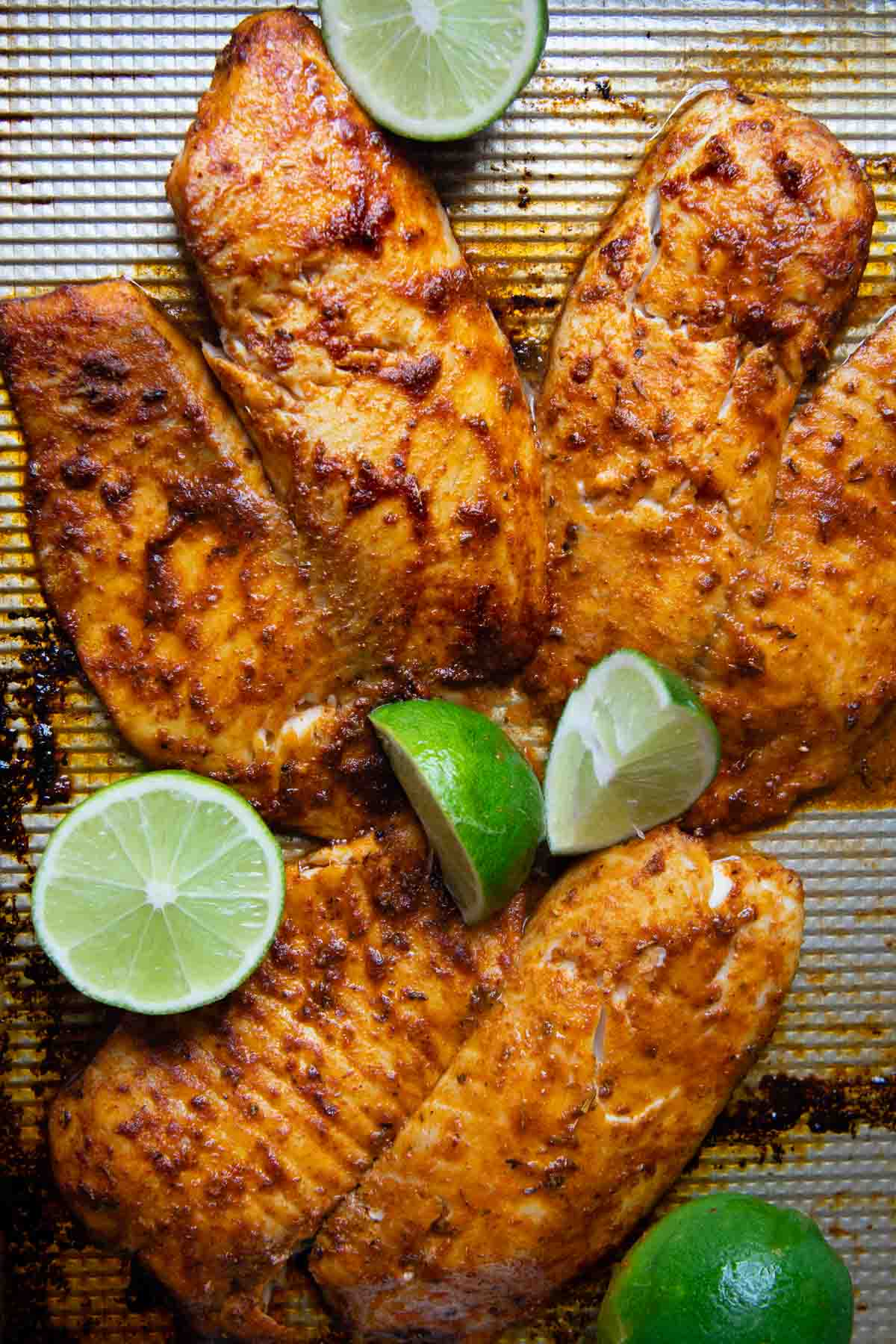 blackened seasoned fish on a baking sheet with limes