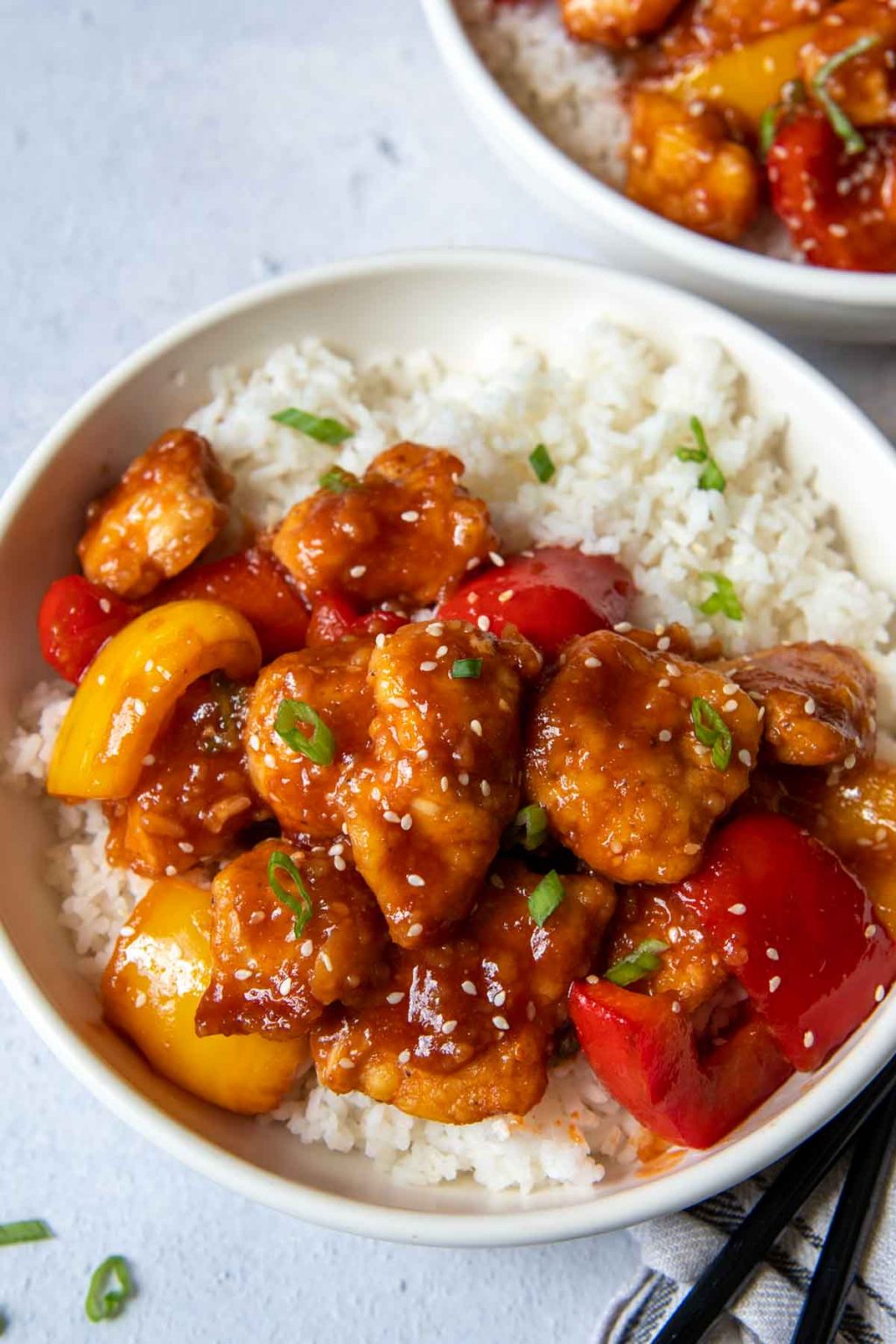 two bowls of sweet sour chicken with chopsticks laying next to it
