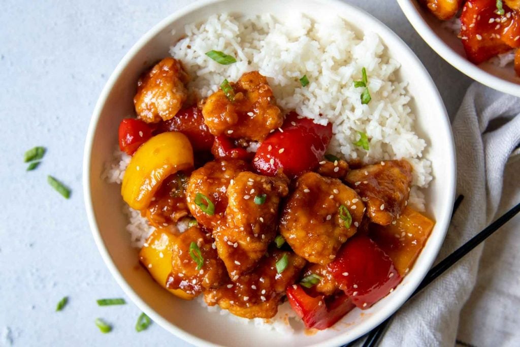 overhead shot of sweet and sour chicken in a white bowl with rice