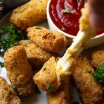a hand pulling the gluten free mozzarella sticks with cheese pulling out