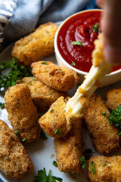 a hand pulling the gluten free mozzarella sticks with cheese pulling out