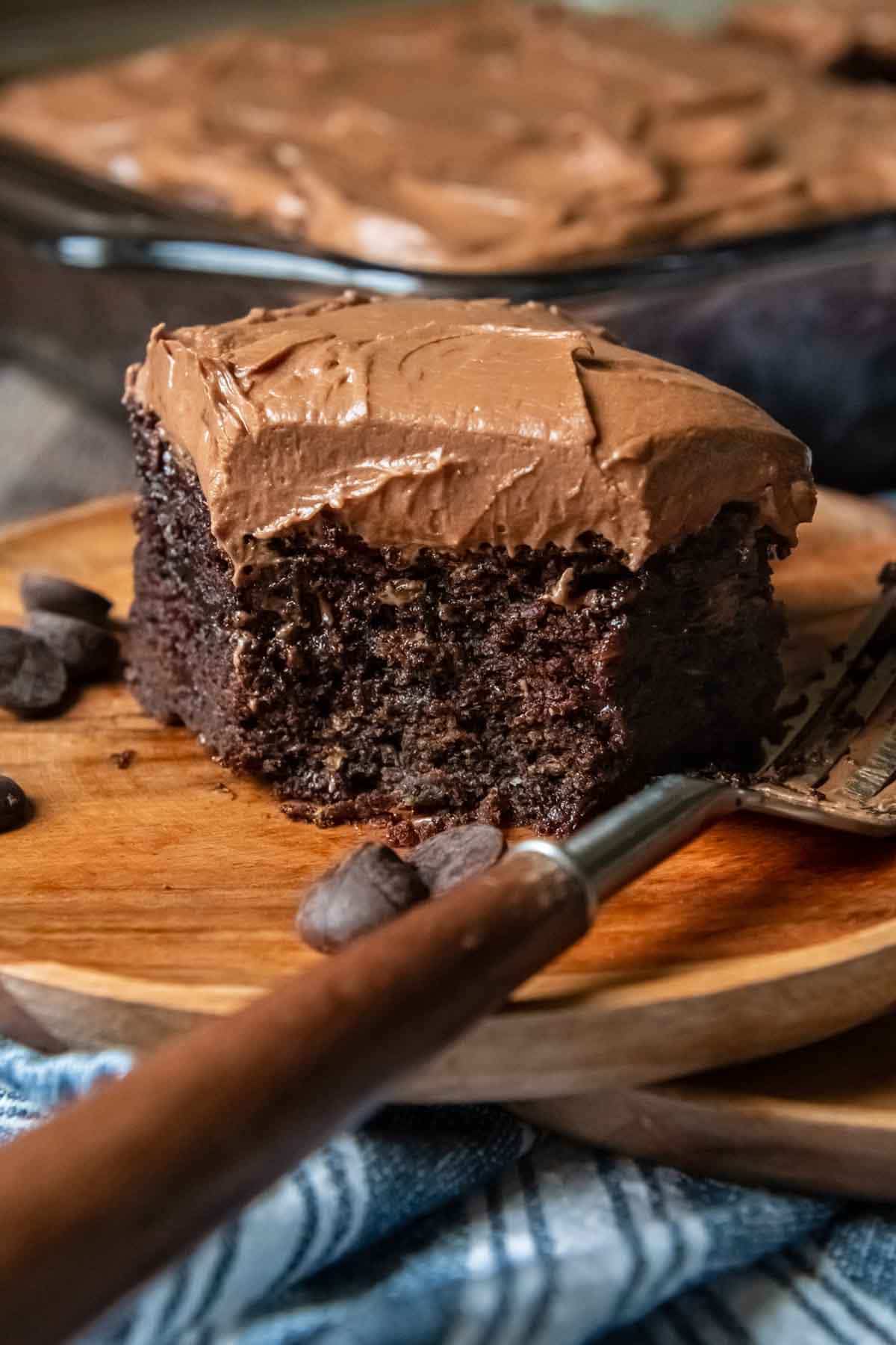 a slice of chocolate cake on a wood plate with a bite taken out