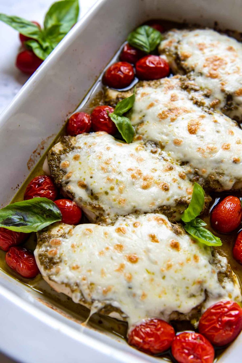 close up of pesto chicken with mozzarella on top in a white baking dish