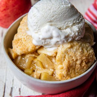 a serving of gluten-free apple cobbler in a white bowl with apples in the back ground