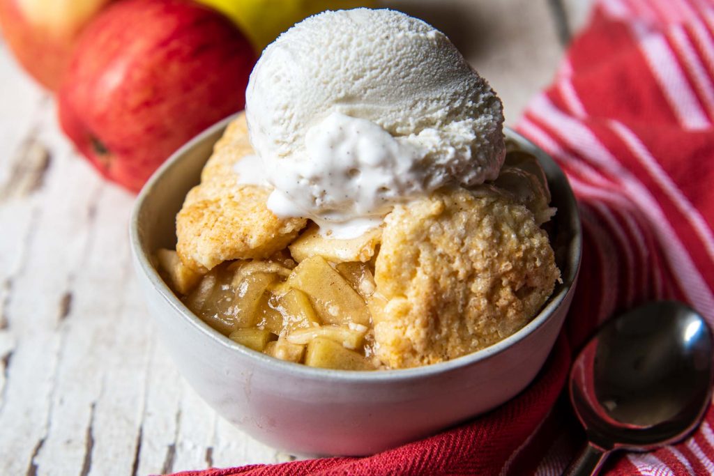 landscape view of apple cobbler in a white bowl with a spoon resting next to it