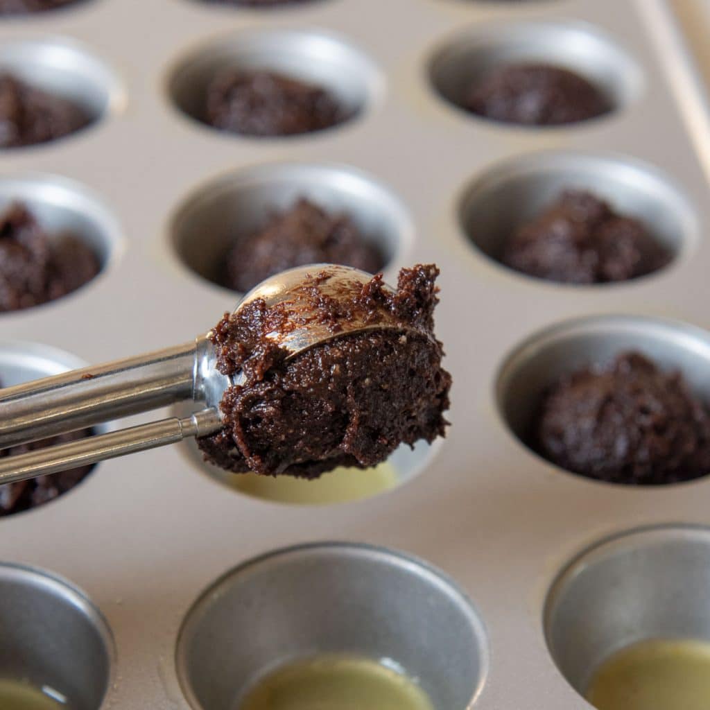a cookie scoop putting uncooked dough in a mini muffin pan