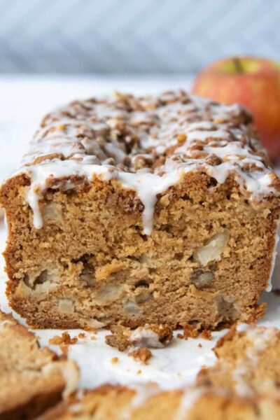 a cut apple bread with apples in the background and frosting dripping down