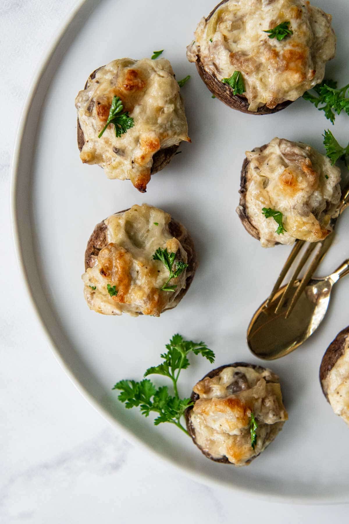 overhead shot of gluten-free stuffed mushrooms on a white plate with gold serving utensils
