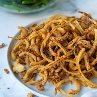 a plate of fried onions with a bowl of green beans behind it