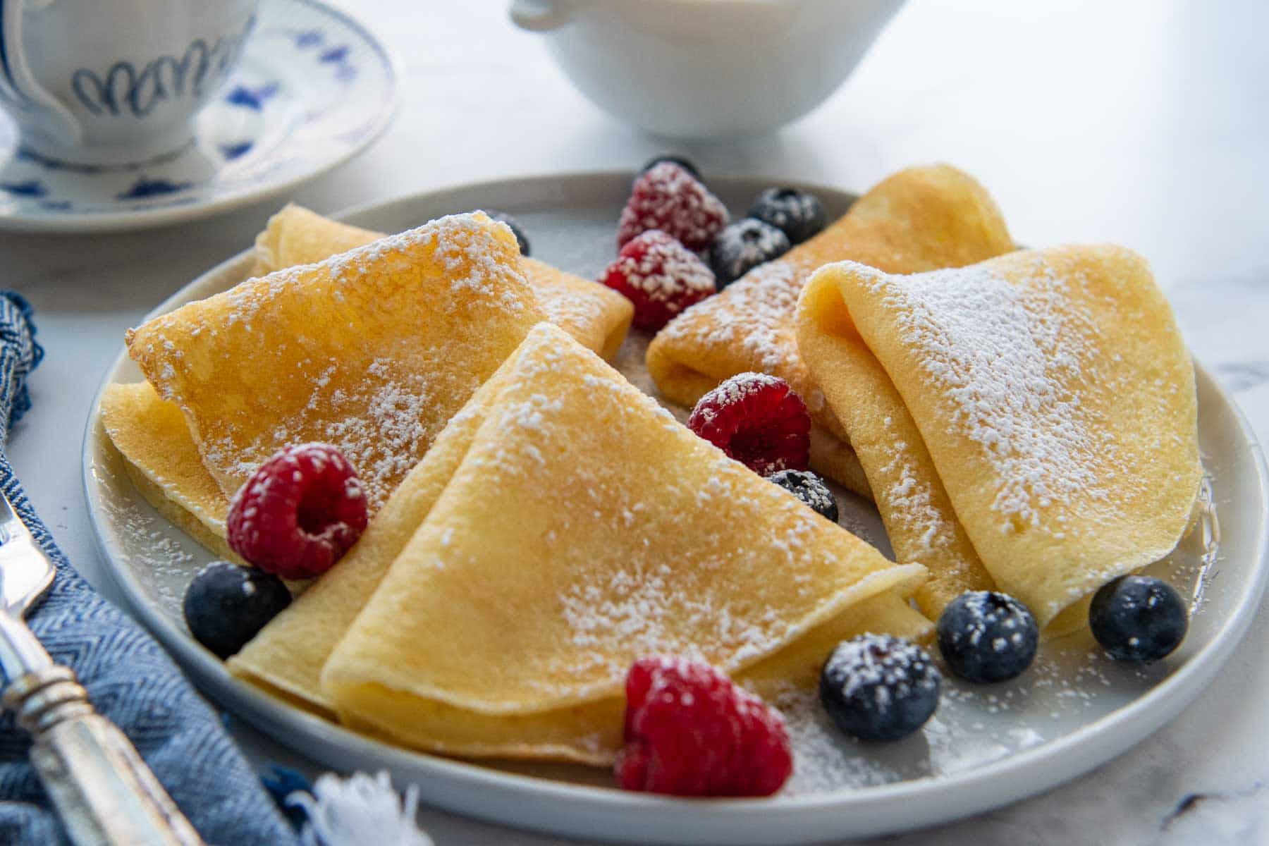 a plate of crepes with powdered sugar and fresh berries