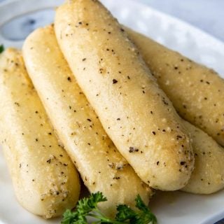 breadsticks stacked on a white plate with parsley