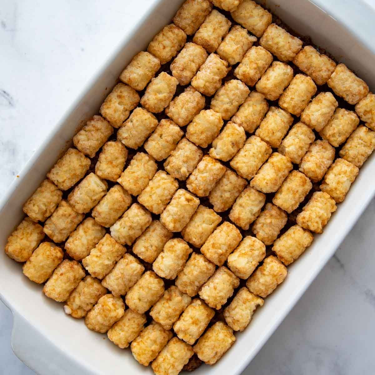 unbaked tater tots lined in a casserole dish.