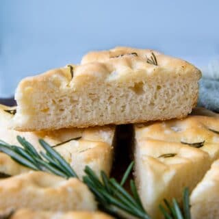a slice of focaccia resting on other slices with fresh rosemary under