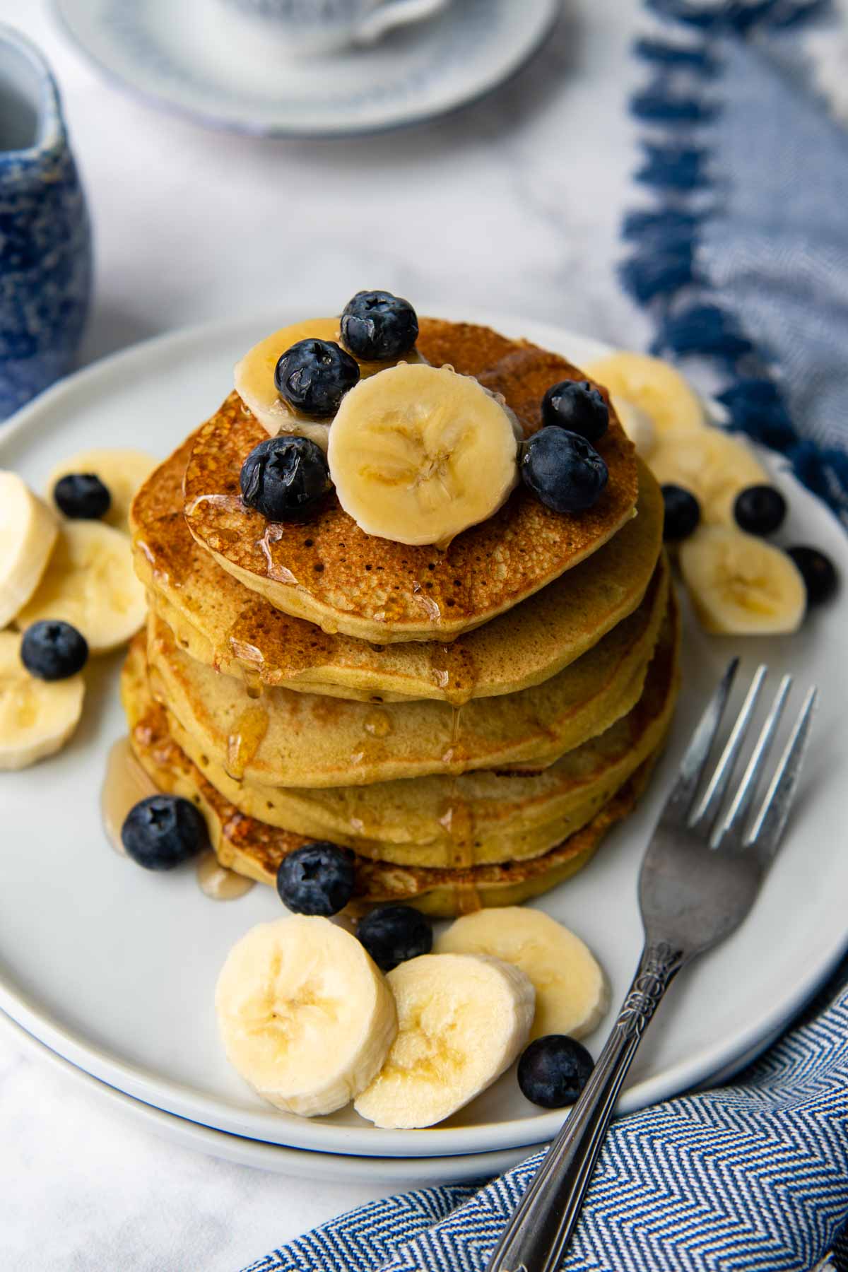 overhead shot of buckwheat pancakes with blueberries and bananas on top.